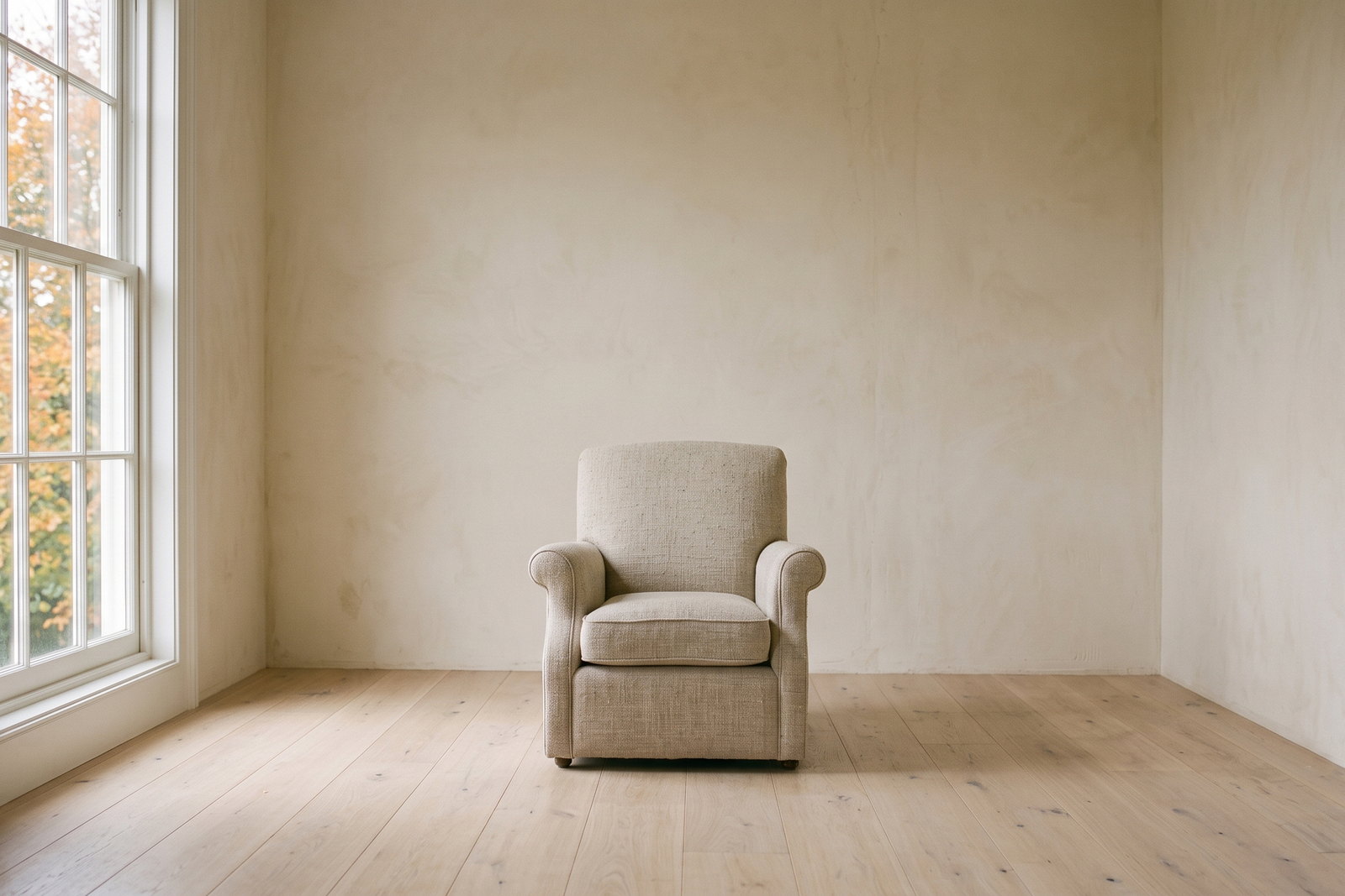 A single upholstered armchair standing alone in an otherwise empty room with pale wood floors and soft daylight.